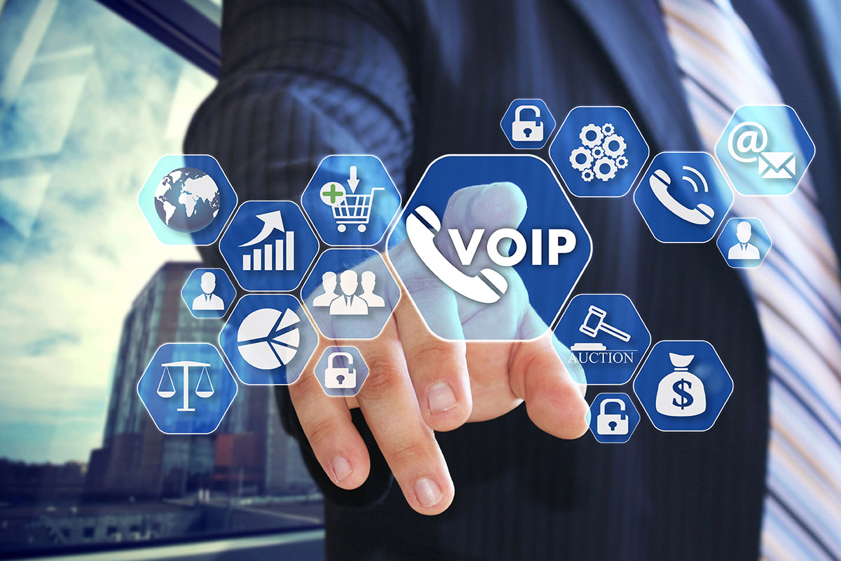 A businessman in a suit is reaching out to touch a virtual interface displaying various icons, including a prominent "VOIP" symbol, along with graphics representing communication, finance, and data analytics. The background features a modern office setting.