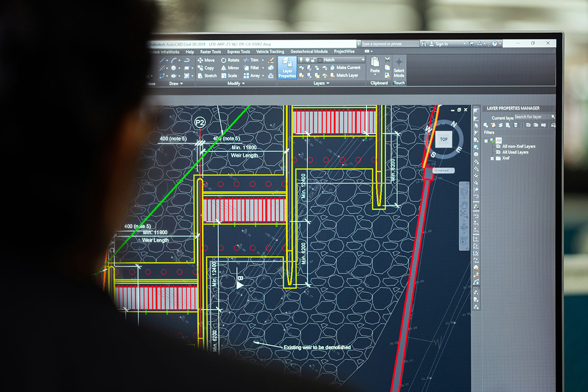 A close-up view of a computer screen displaying a technical drawing in AutoCAD, showing detailed design elements such as measurements, lines, and layers related to a construction project, with a person partially visible in the foreground.